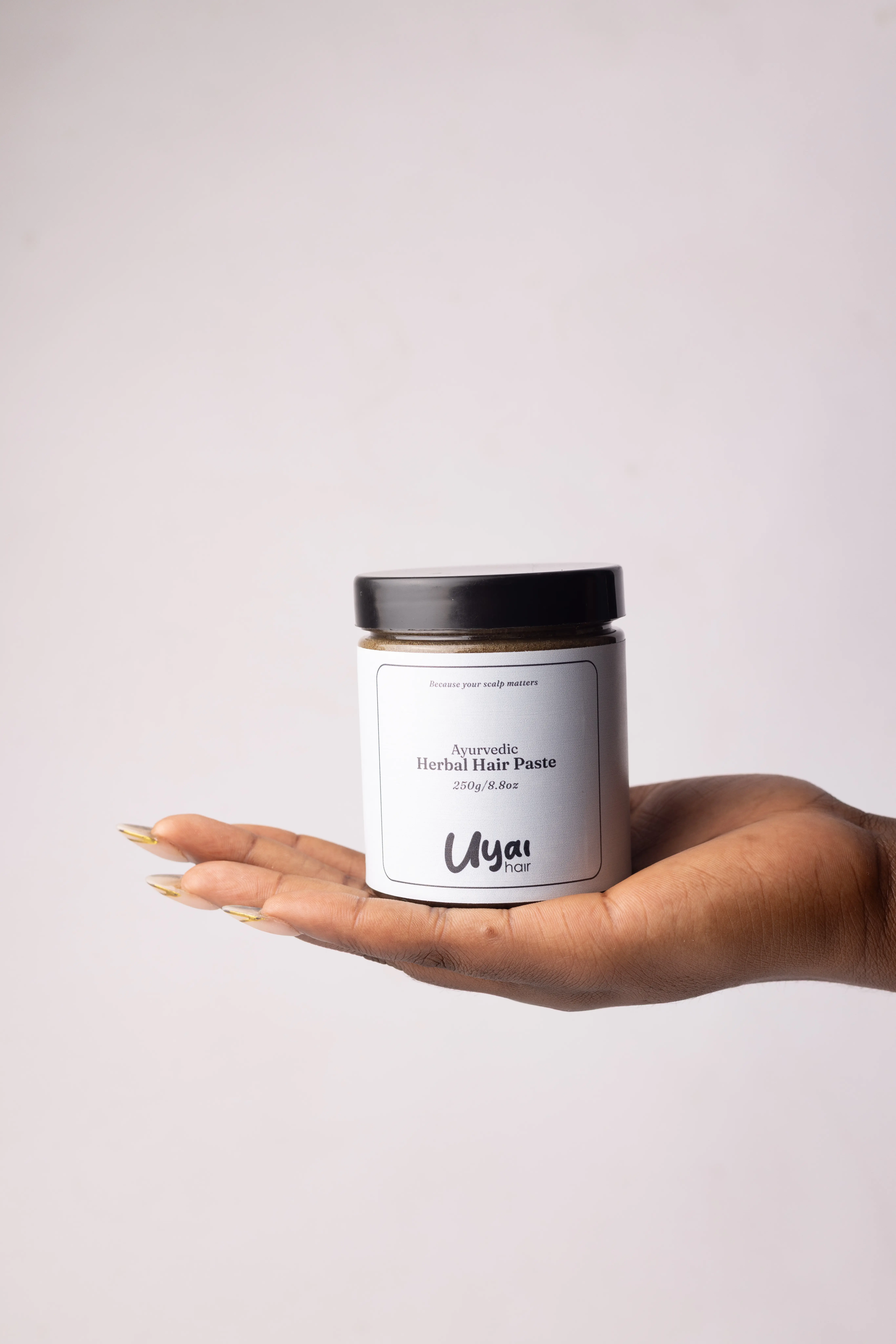 Hand holding Uyai Hair Herbal Hair Paste sealed container